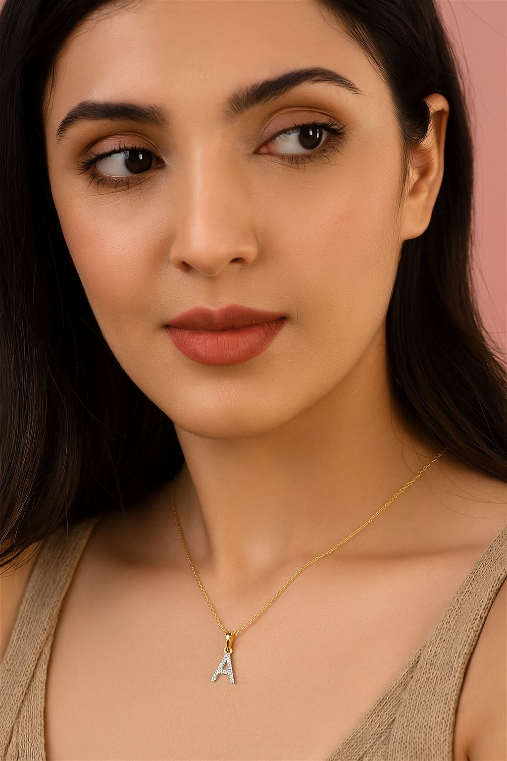 Woman wearing a gold necklace with an 'A' pendant against a pink background