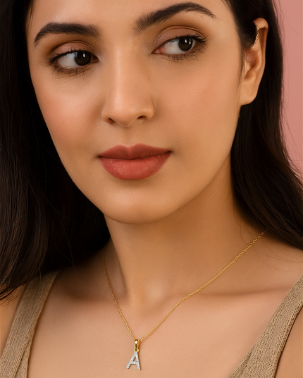Woman wearing a gold necklace with an 'A' pendant against a pink background