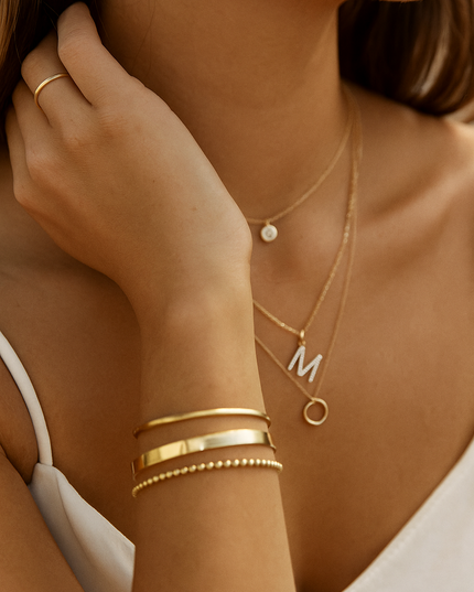 Close-up of a person wearing gold jewelry including necklaces, bracelets, and a ring.